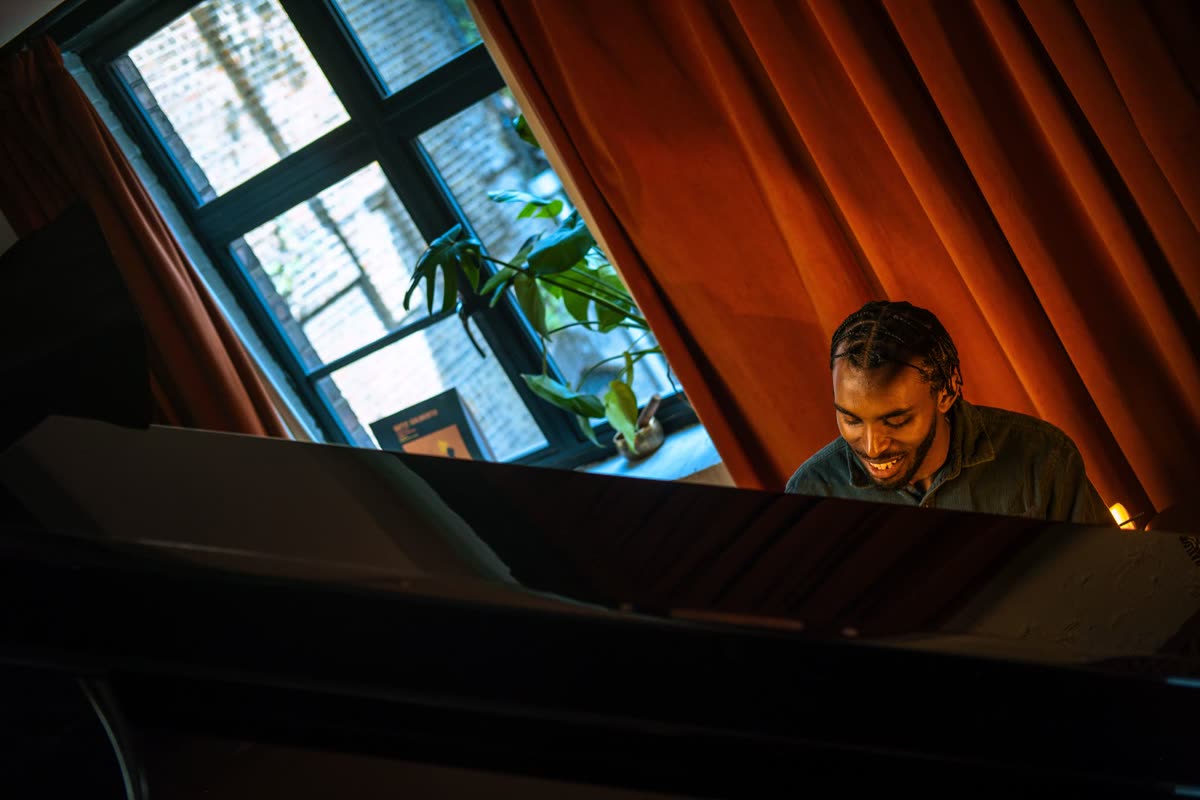 Judah smiling at a grand piano by a window with red curtains