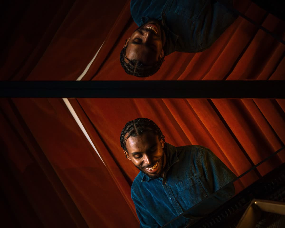 Judah reflected in the raised lid of a grand piano, red curtains behind